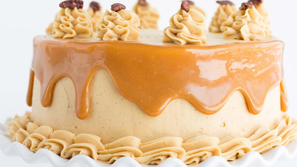 Round cake with caramel glaze dripping over the sides, topped with piped swirls of frosting and pecan halves&mdash;an elegant choice for Easter desserts&mdash;presented on a white cake stand.