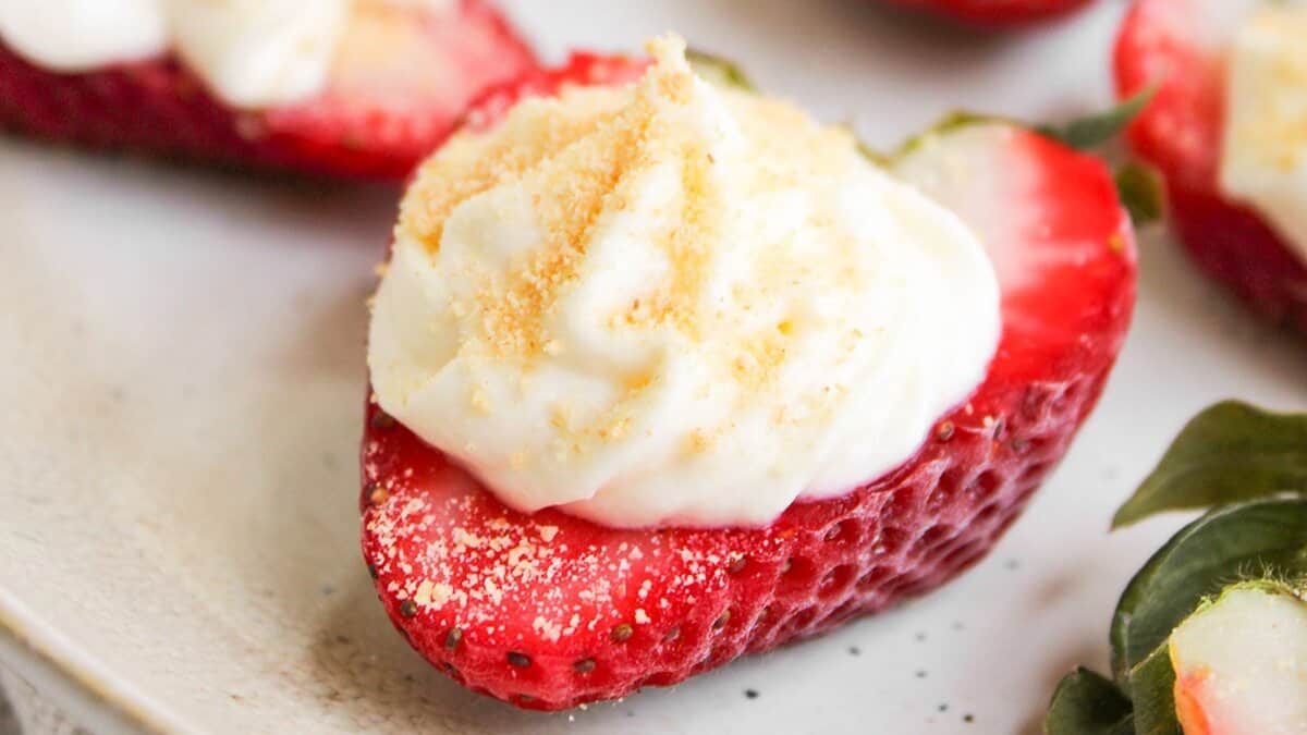 A halved strawberry filled with a dollop of whipped cream and sprinkled with crumbs, this elegant mini dessert is perfect for spring parties, served on a white plate.