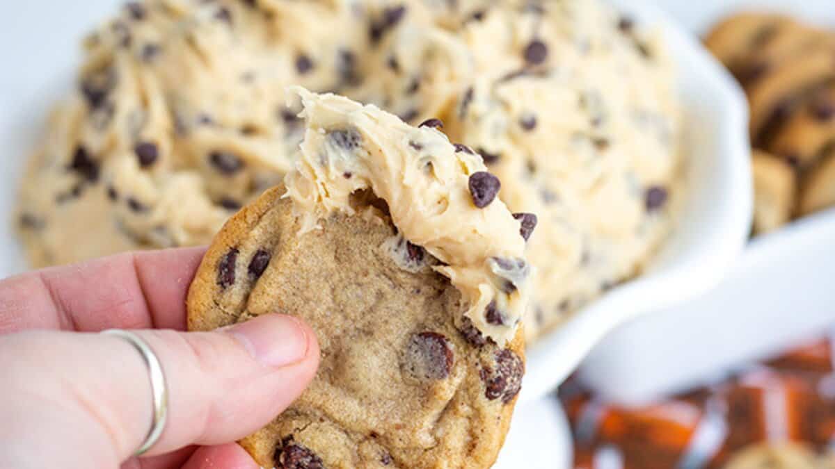 A hand holding a chocolate chip cookie with a scoop of chocolate chip cookie dough in front of a bowl filled with more easy, no bake desserts&mdash;perfect for satisfying your sweet tooth all winter long.