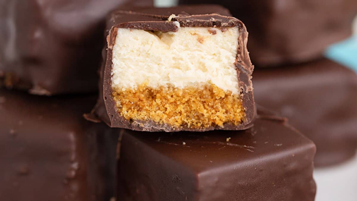 A close-up of chocolate-coated cheesecake bites with a visible graham cracker crust and creamy cheesecake layer inside—perfect mini desserts for spring parties.