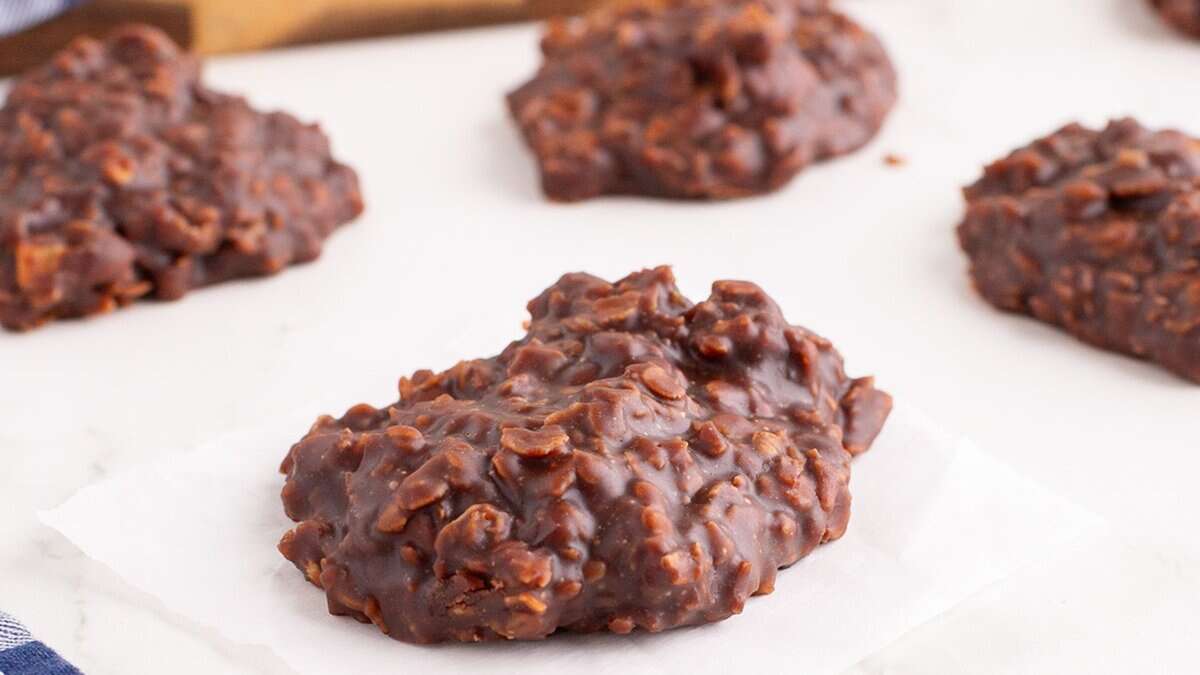 A no-bake chocolate oatmeal cookie rests on parchment paper—perfect for mini desserts at spring parties—with additional cookies blurred in the background on a white surface.