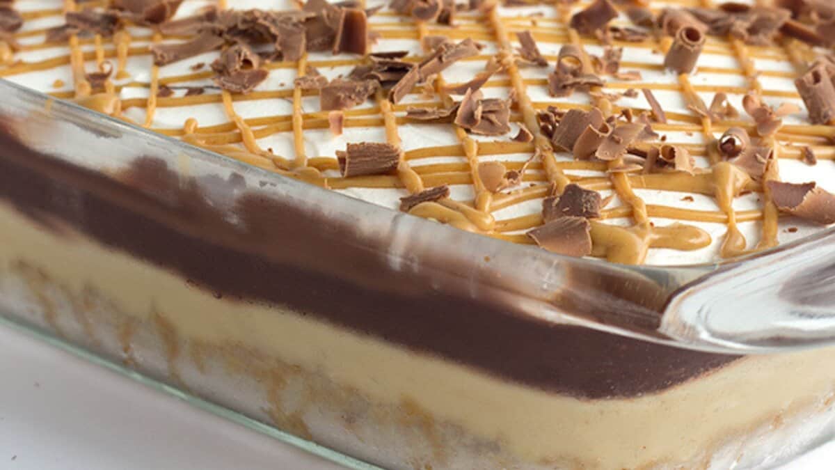 A glass dish filled with a no bake dessert, featuring a creamy base, chocolate layer, whipped topping, caramel drizzle, and chocolate shavings&mdash;an easy dessert perfect for winter desserts.