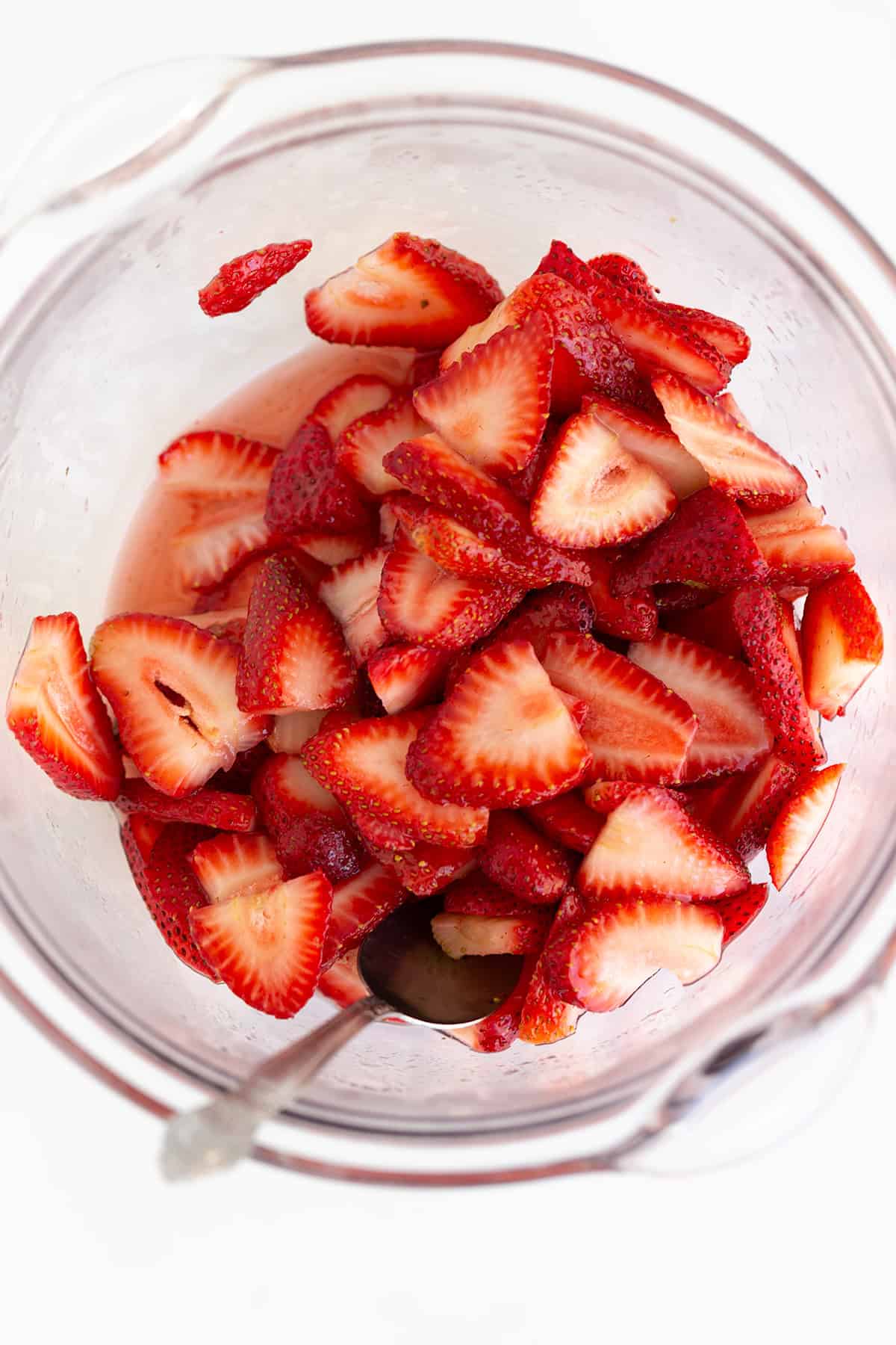 Sliced strawberries in a glass bowl with a spoon, photographed from above&mdash;perfect for a light dessert or as a topping for strawberry shortcake.