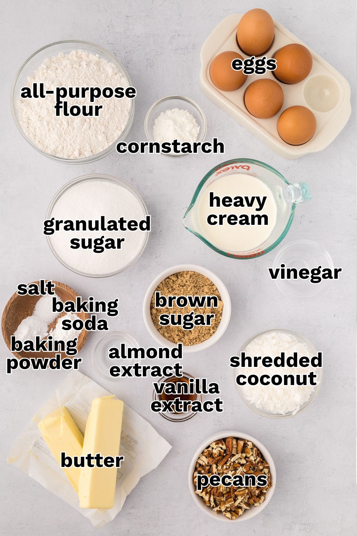 Various baking ingredients for Italian Cream Cake, including eggs, flour, cornstarch, heavy cream, granulated and brown sugar, vinegar, coconut, pecans, butter, extracts, baking powder, baking soda, and salt.