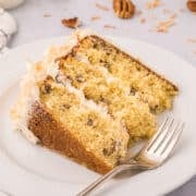 A slice of three-layer Italian Cream Cake with white frosting on a white plate, garnished with shredded coconut and pecans, with a fork beside it.