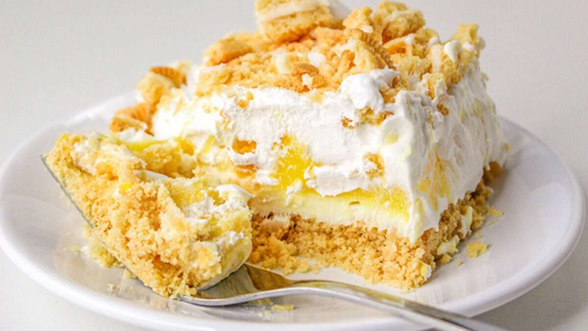 A slice of layered lemon dessert topped with whipped cream and crumbled cookies is served on a white plate with a fork&mdash;one of the best no bake desserts for easy, sweet indulgence.