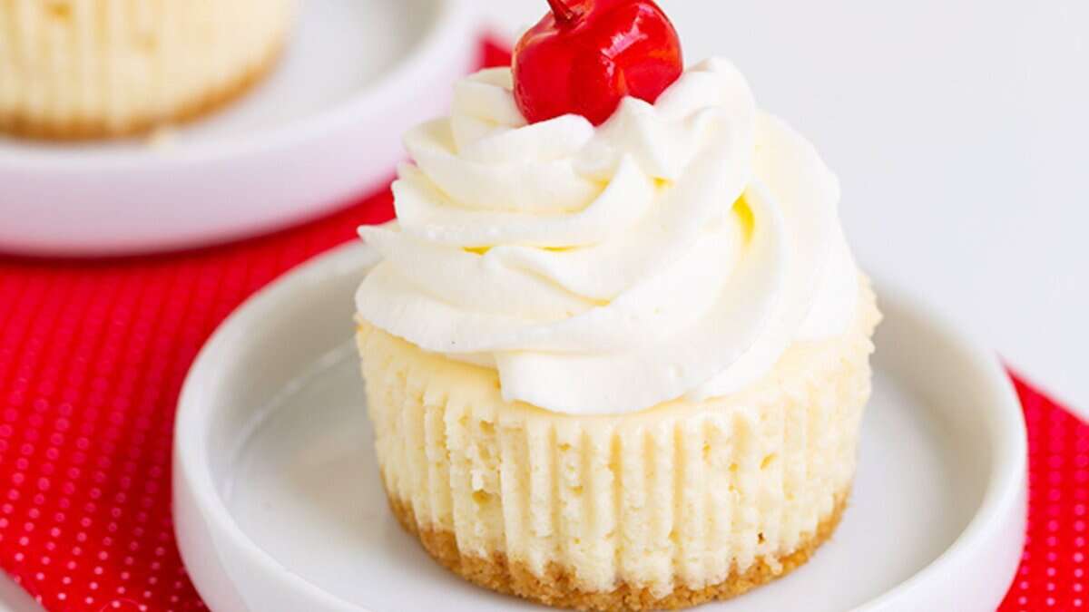 A mini cheesecake topped with swirled whipped cream and a cherry, served on a white plate—perfect for spring parties and ideal among mini desserts.