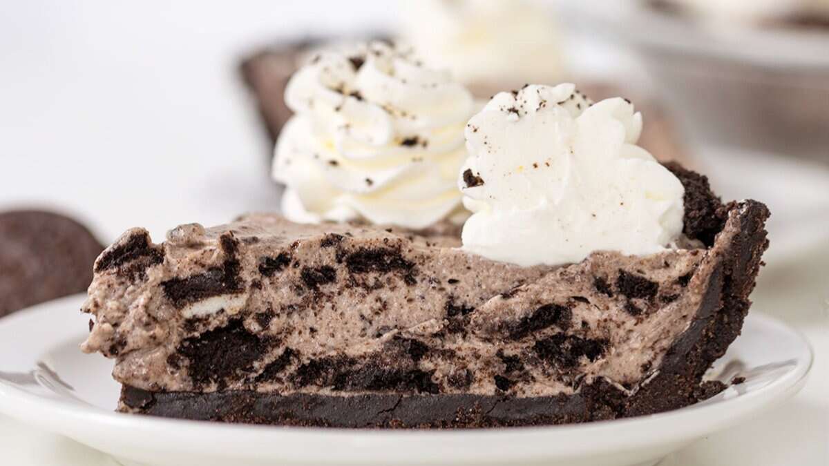 A slice of cookies and cream pie with crushed cookies in the filling, topped with whipped cream, on a white plate&mdash;one of the easiest no bake desserts for sweet cravings.