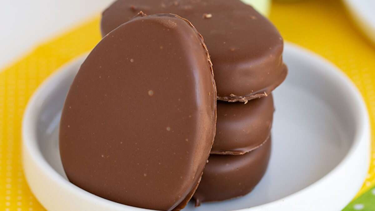 Three chocolate-covered oval-shaped candies are stacked on a small white plate, with a yellow surface underneath&mdash;perfect for adding to your Easter desserts spread.