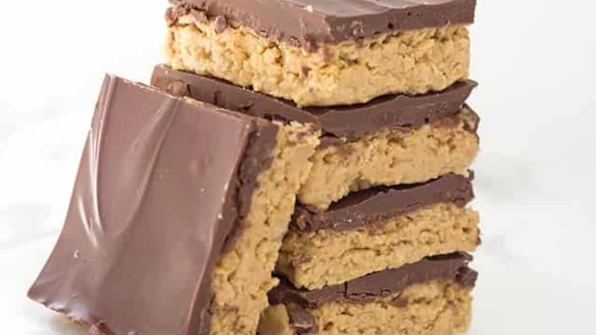 A stack of five chocolate-topped peanut butter bars, perfect for easy desserts, with one bar leaning against the stack on a white surface.