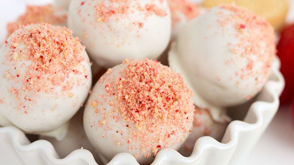 A bowl of mini desserts featuring white chocolate-coated truffles, topped with pink crushed strawberry crumbs—perfect for spring parties.