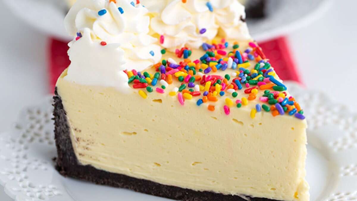 A slice of cheesecake with a chocolate cookie crust, topped with whipped cream and colorful rainbow sprinkles, on a white plate&mdash;a perfect choice for easy desserts and no bake desserts lovers.