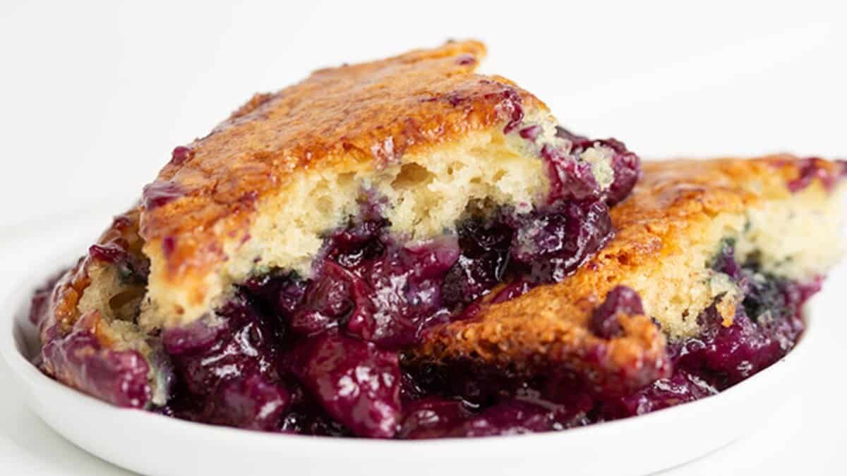 A close-up of a blueberry cobbler with a golden-brown crust and juicy blueberry filling, served on a white plate&mdash;one of the best easy desserts for those seeking stress-free desserts.