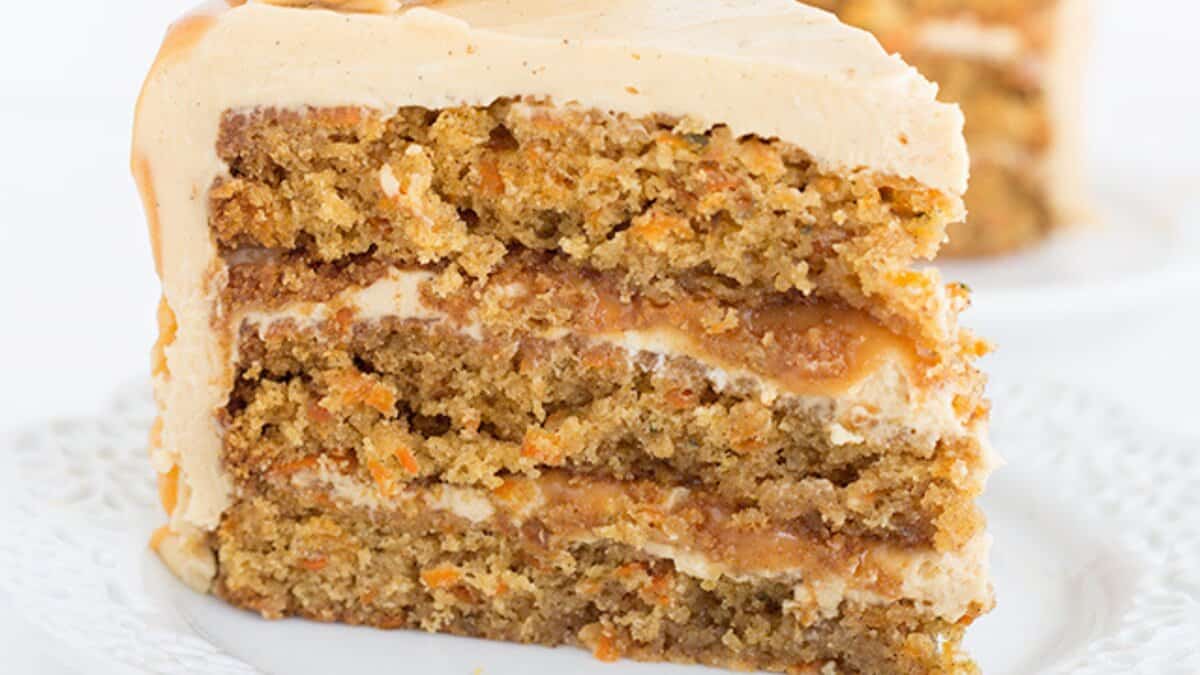 A slice of layered carrot cake with cream cheese frosting on a white plate&mdash;one of those classic desserts everyone loves.
