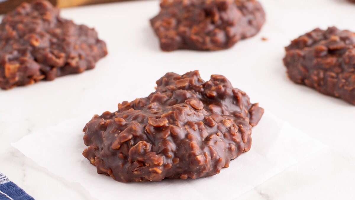 A no-bake chocolate oatmeal cookie sits on a piece of parchment paper, with more cookies in the background on a white surface&mdash;an ideal choice for easy desserts and simple dessert recipes.