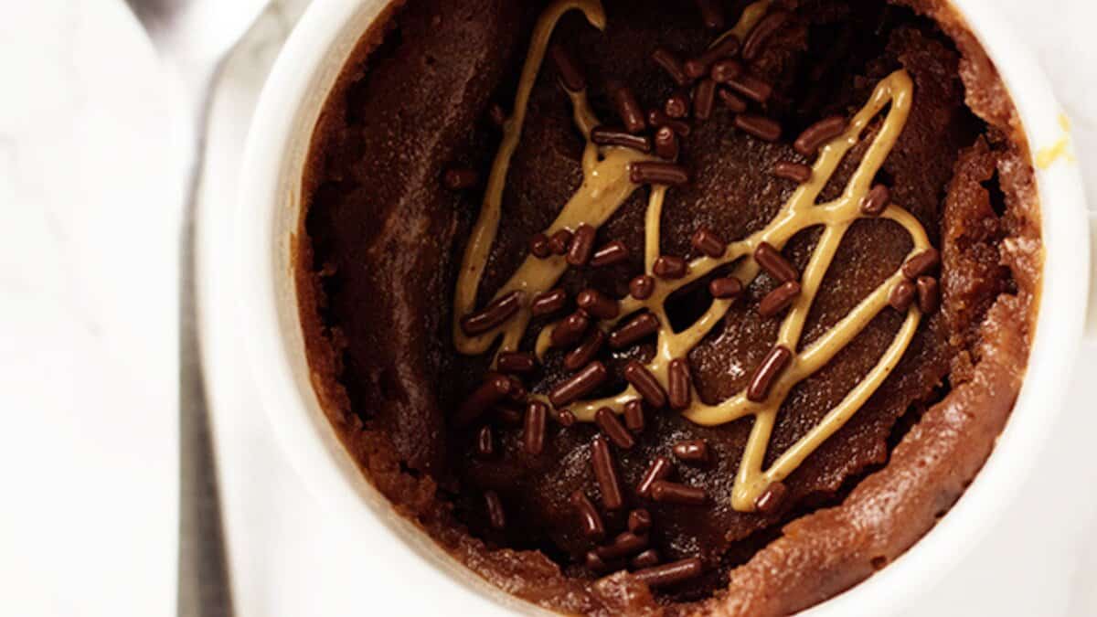 Chocolate mug cake topped with a drizzle of peanut butter and chocolate sprinkles, served in a white mug&mdash;perfect for fans of easy desserts and stress-free desserts.