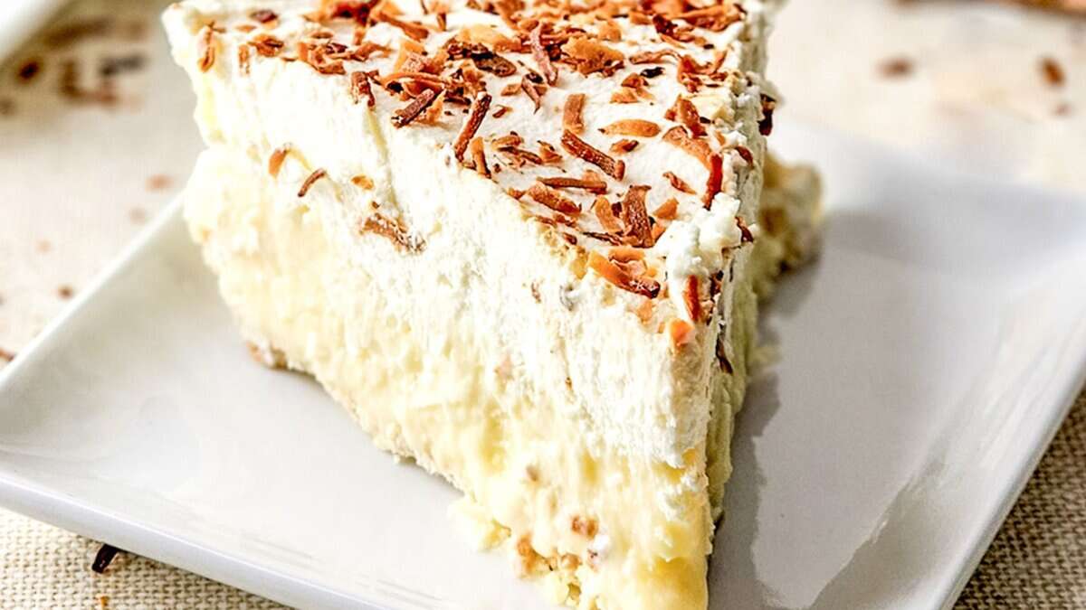 A slice of coconut cream pie topped with toasted coconut flakes on a white plate&mdash;a true favorite among classic desserts.