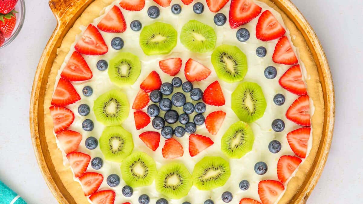 A fruit pizza topped with sliced kiwis, strawberries, and blueberries arranged in concentric circles on a round crust&mdash;one of the best easy desserts for any occasion.