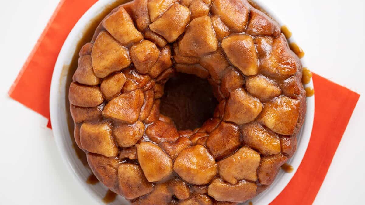 A round monkey bread with glazed, pull-apart pieces sits on a white plate over an orange napkin&mdash;a perfect example of stress-free desserts anyone can make.