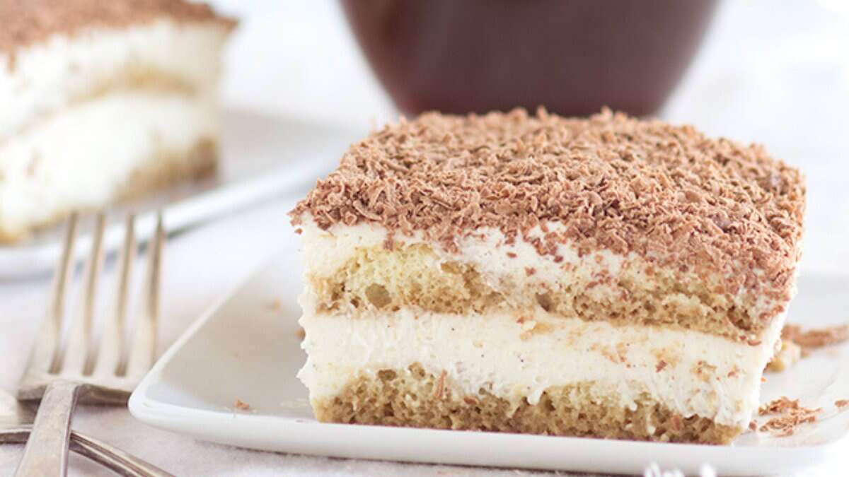 A slice of tiramisu on a white plate, showing layers of cream and cake, topped with grated chocolate, with a fork beside it&mdash;a classic choice for easy desserts.