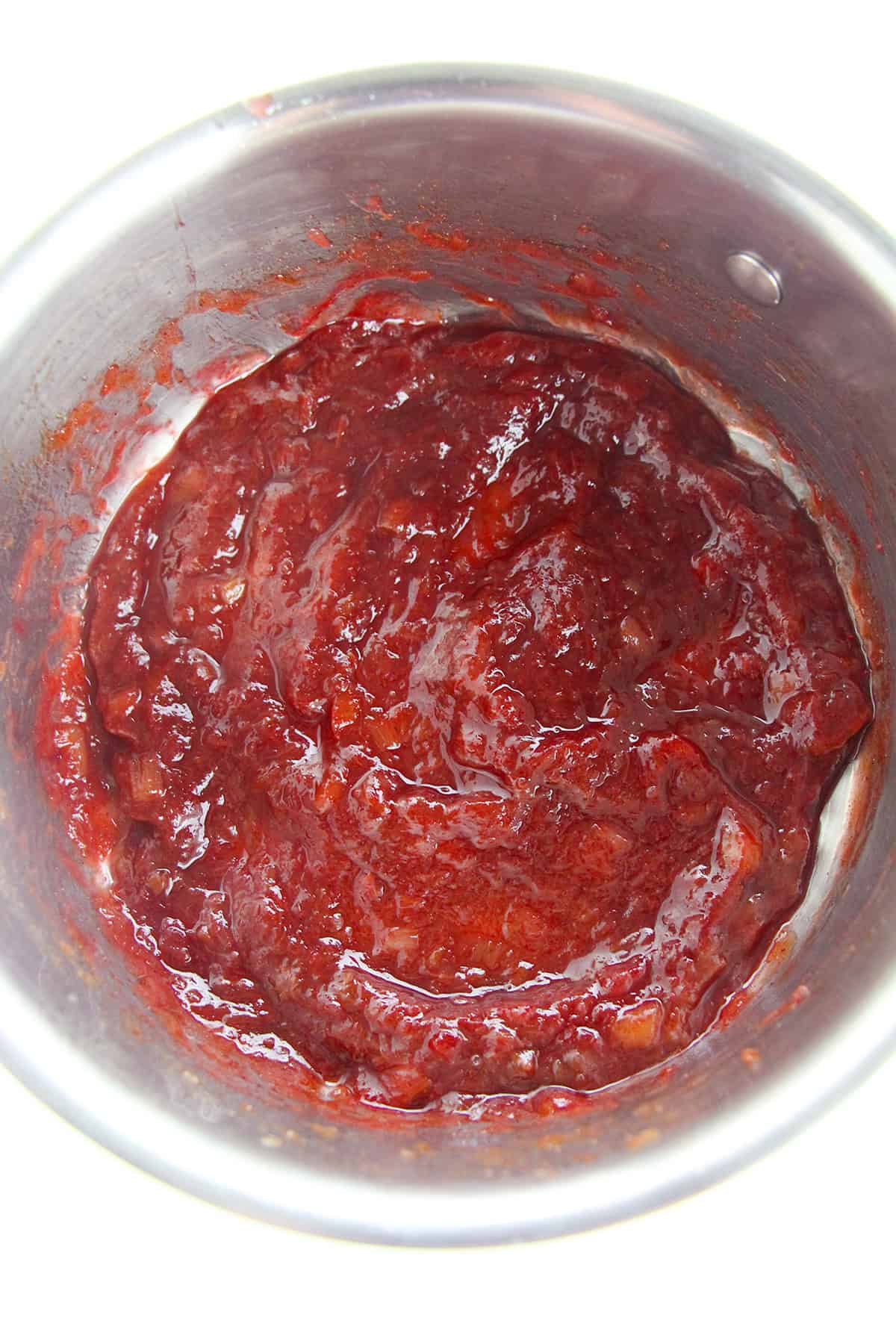 A stainless steel pot containing thick, chunky red stewed rhubarb, likely a delicious stewed fruit or rhubarb recipe made from cooked tomatoes or berries.