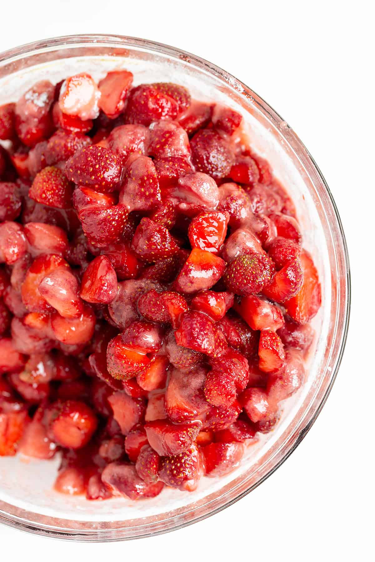 A glass bowl filled with chopped strawberries coated in a glossy mixture, viewed from above on a white background&mdash;perfectly prepped for an Easy Strawberry Cobbler.