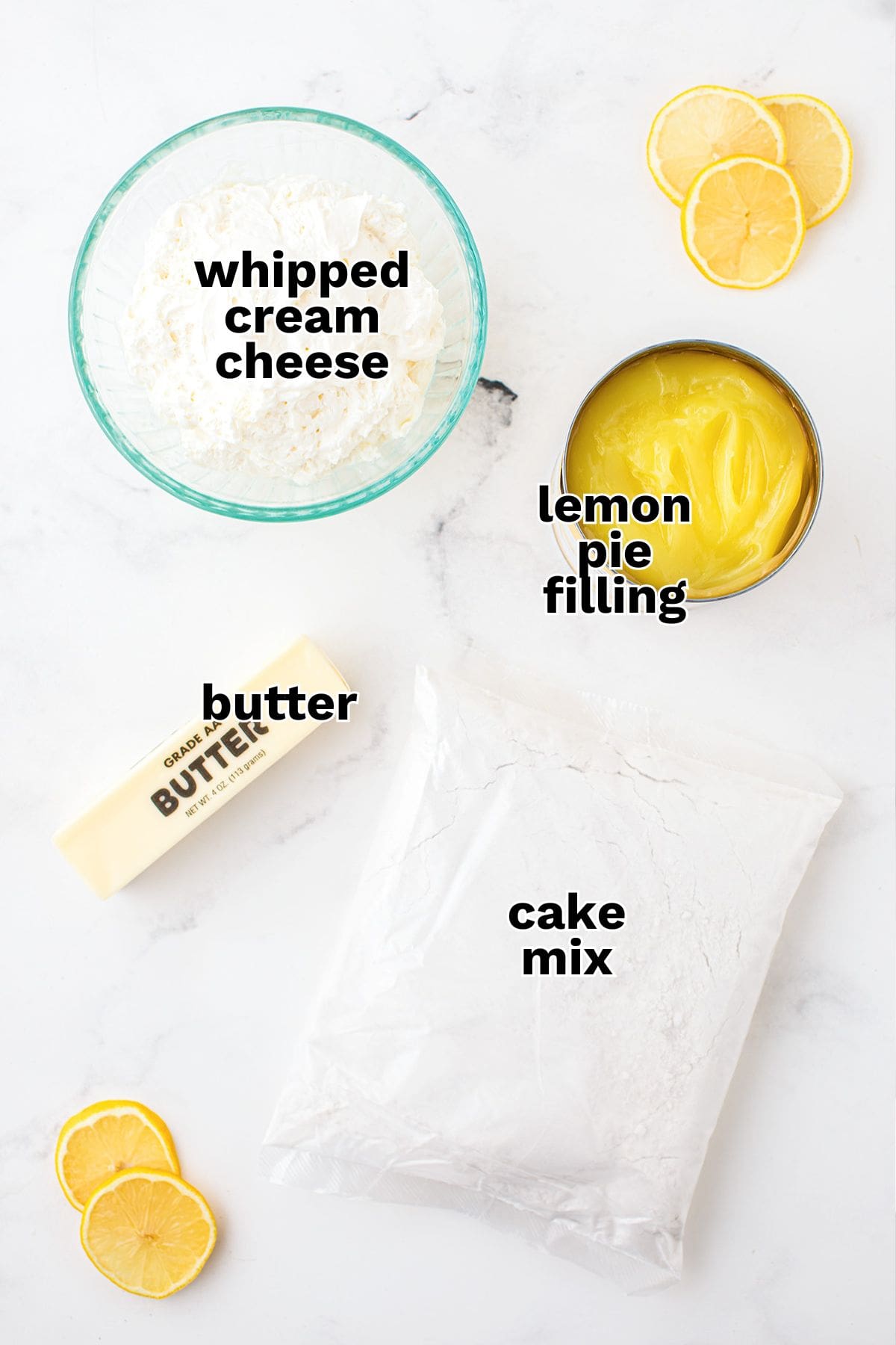 Top-down view of four baking ingredients for a lemon dump cake: whipped cream cheese in a bowl, lemon pie filling in a can, a stick of butter, and cake mix, with fresh lemon slices nearby.