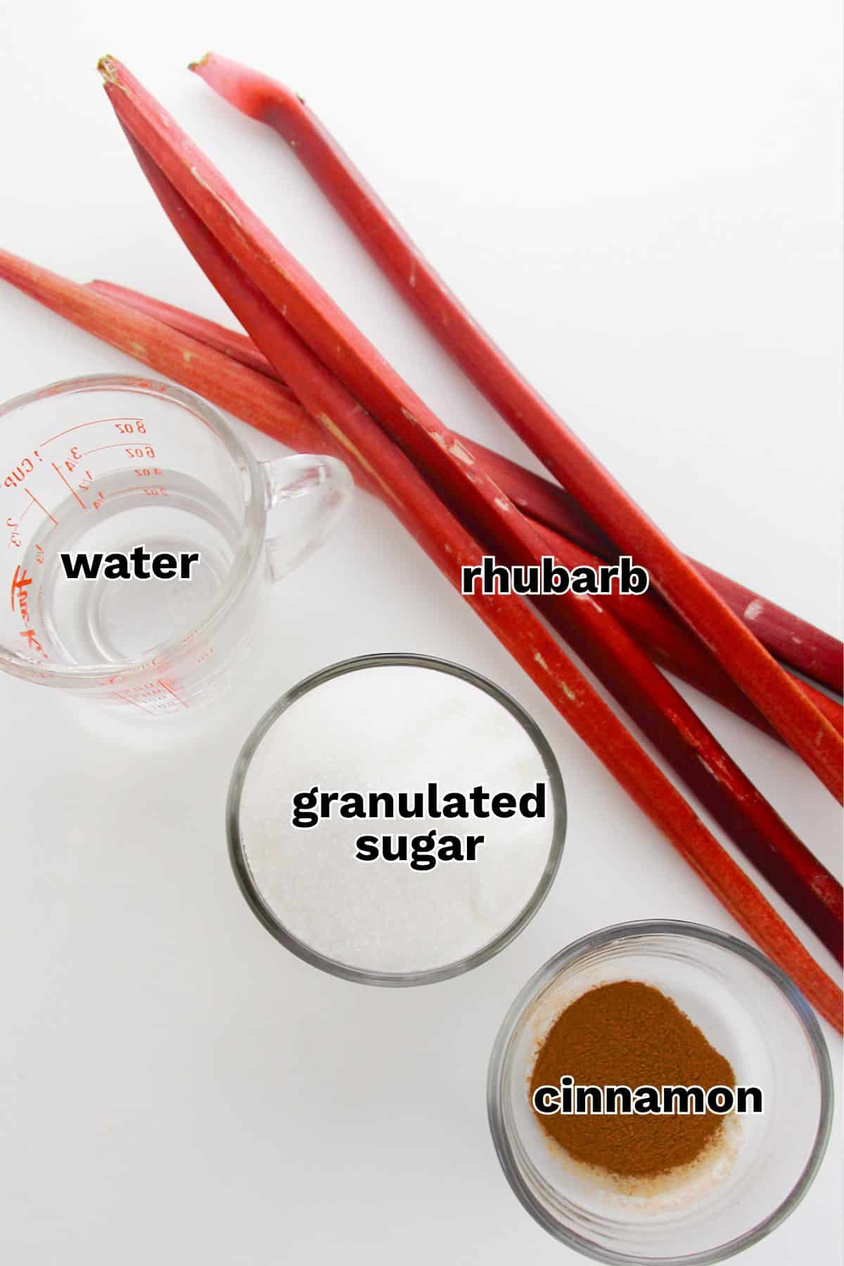 Overhead view of rhubarb stalks, a measuring cup of water, a bowl of granulated sugar, and a small bowl of ground cinnamon&mdash;classic ingredients for a delicious stewed rhubarb recipe on a white surface.