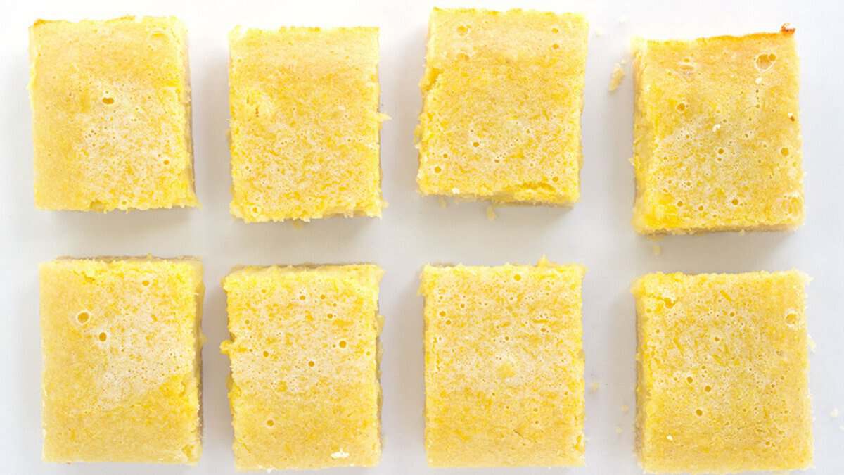 Eight square pieces of yellow cake or bars, a delightful example of classic desserts, are arranged in two rows on a white surface.