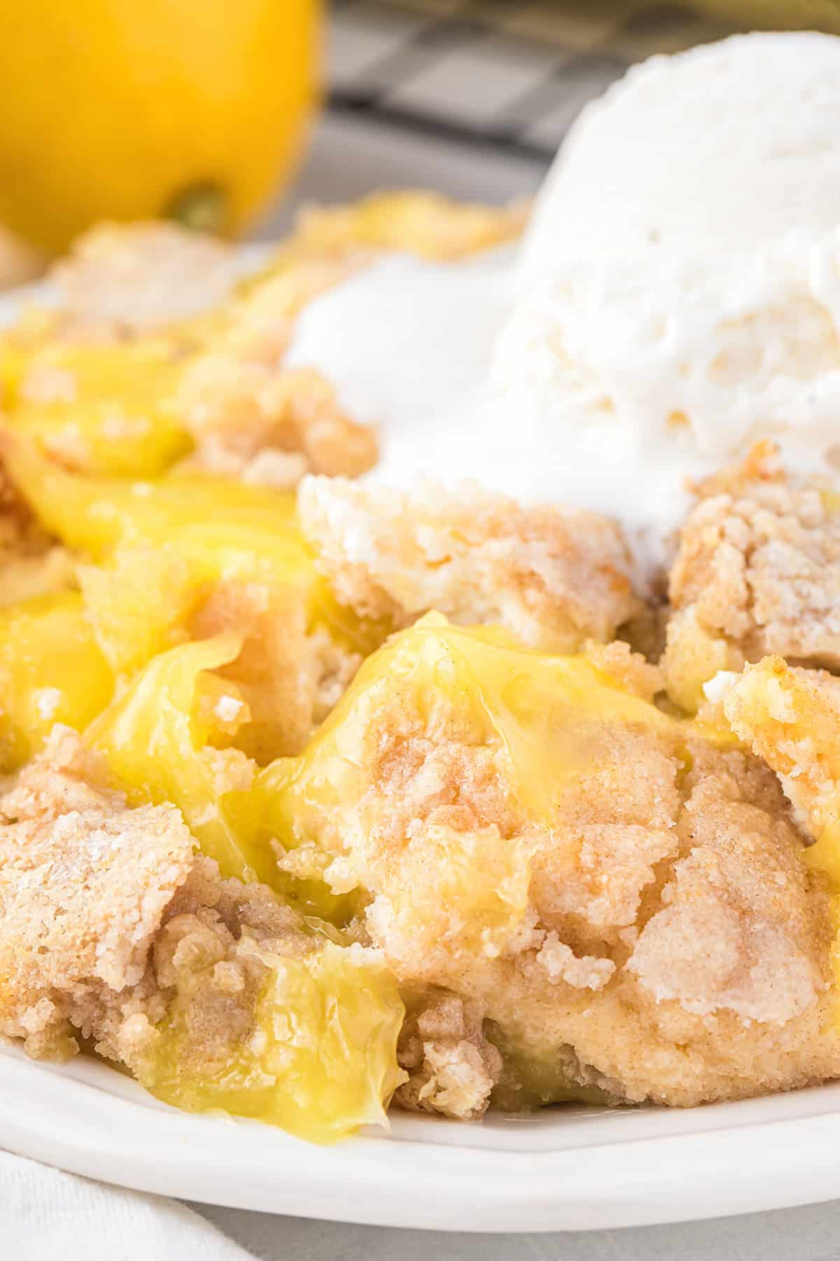 A close-up of lemon cobbler, a delightful lemon dessert, topped with a scoop of vanilla ice cream on a white plate.
