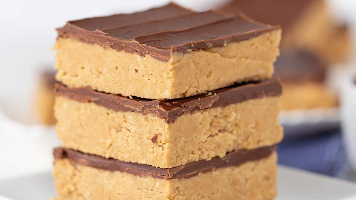 Three stacked peanut butter bars with a thick chocolate layer on top, displayed on a white plate&mdash;these classic desserts are the perfect blend of rich flavor and timeless appeal.