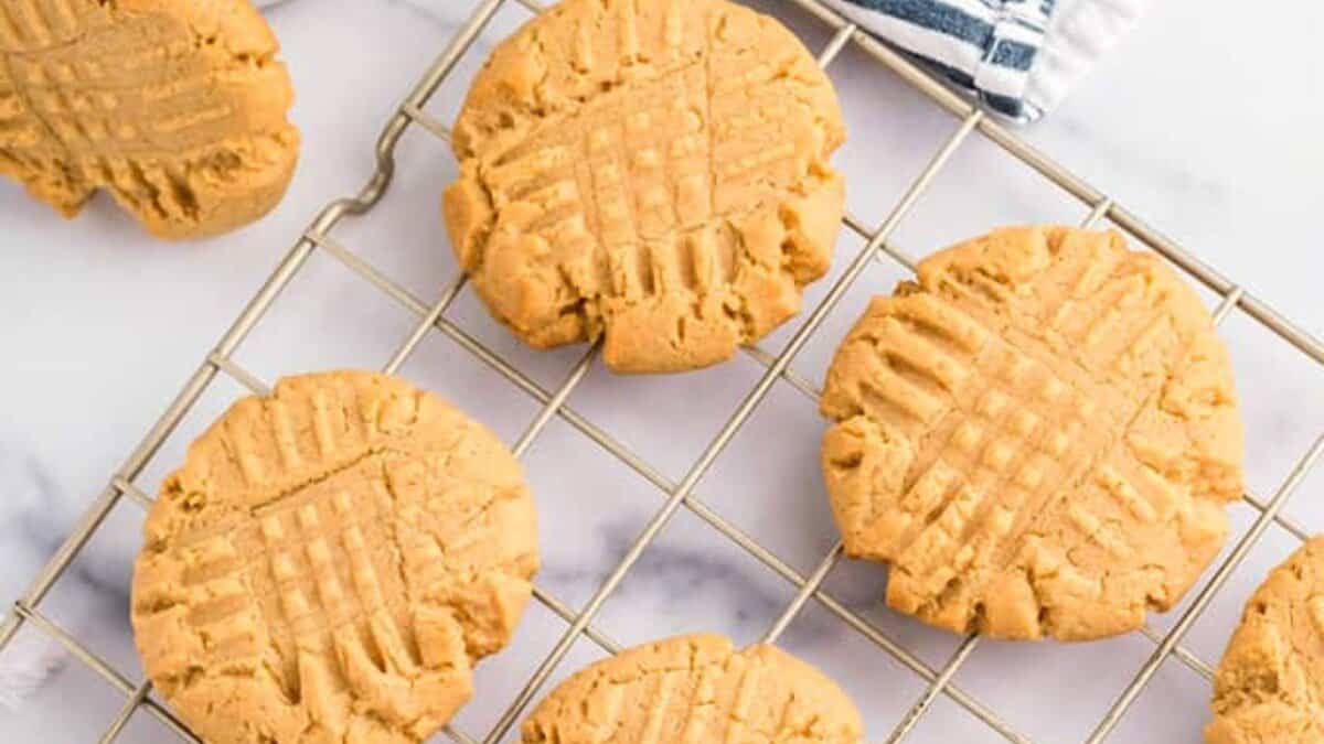 Six peanut butter cookies with crisscross fork marks are cooling on a wire rack placed on a marble surface&mdash;easy desserts anyone can make for a stress-free treat.