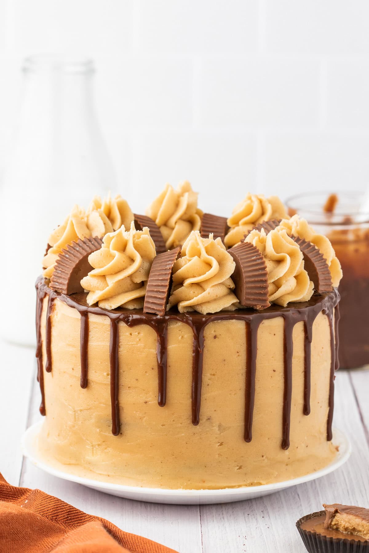 A frosted peanut butter chocolate cake with chocolate ganache drip, decorated with swirls of icing and halved peanut butter cups on top, set on a white plate.