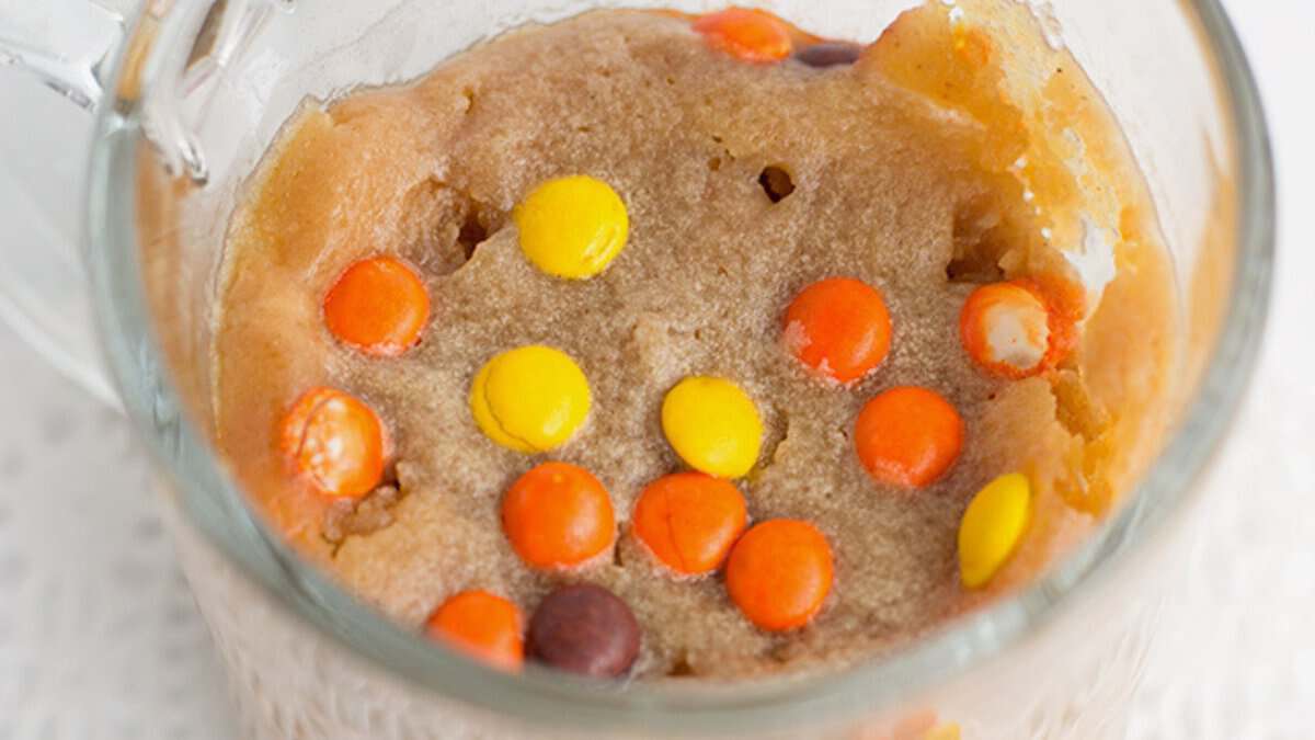 A stress-free dessert, this peanut butter mug cookie is topped with orange, yellow, and brown candy-coated chocolates and served in a glass mug.