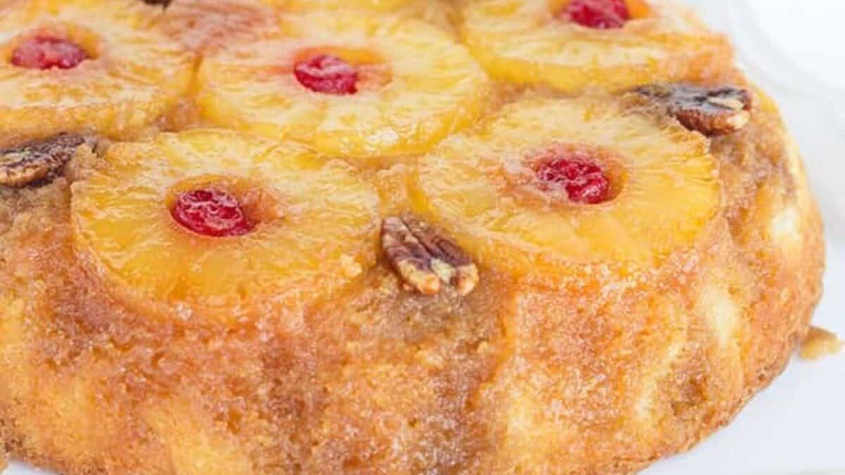 A classic dessert, this pineapple upside-down cake features pineapple rings, maraschino cherries, and pecan halves arranged on a white surface.