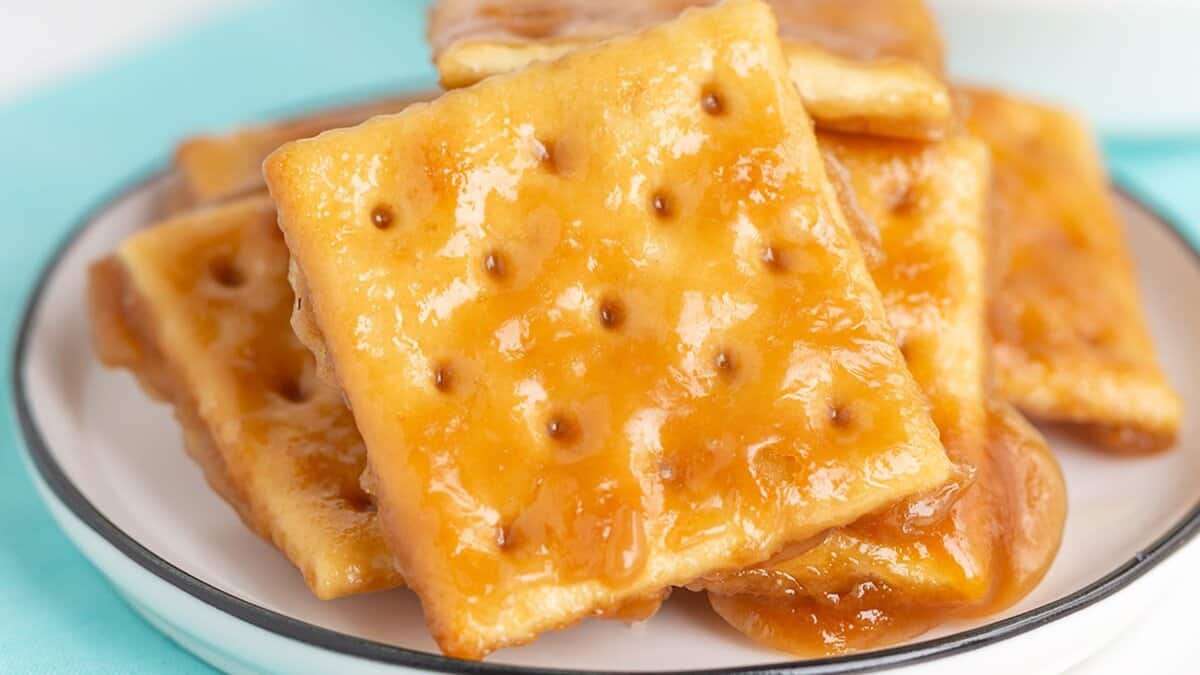 A stack of square crackers coated in a glossy caramel sauce sits on a white plate with a black rim, making for one of those easy desserts perfect for stress-free entertaining.