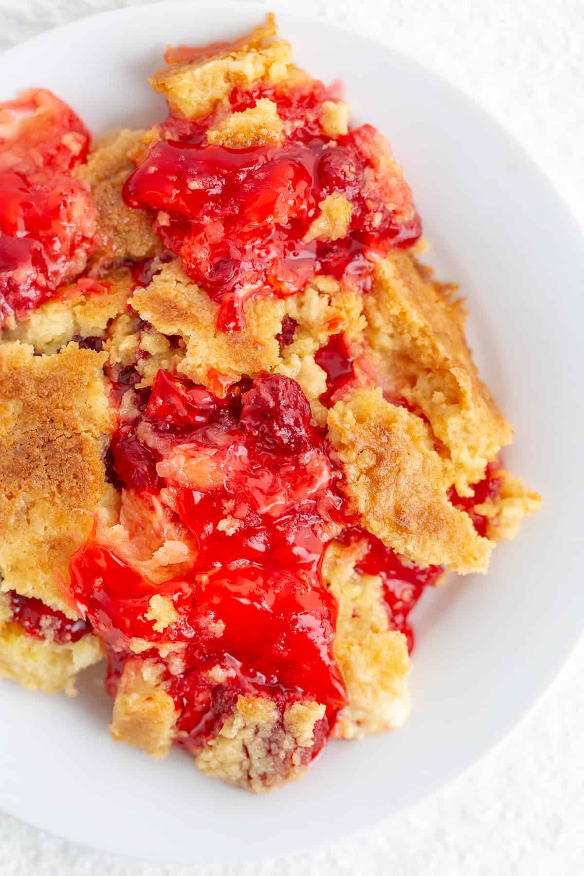 A serving of cherry dump cake with a golden, crumbly topping and bright red cherry filling, perfect for pairing with sweet pineapple or strawberry flavors, on a white plate.