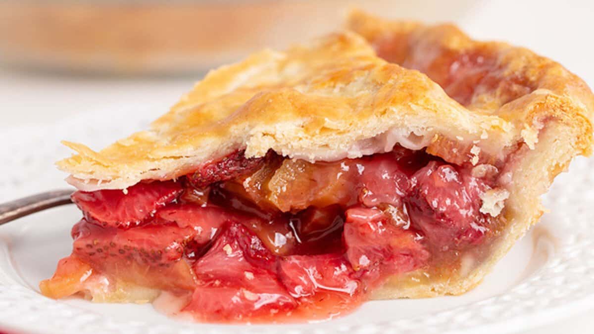 A slice of strawberry pie with a golden, flaky crust and a filling of glazed strawberries on a white plate&mdash;a delightful example of classic desserts.