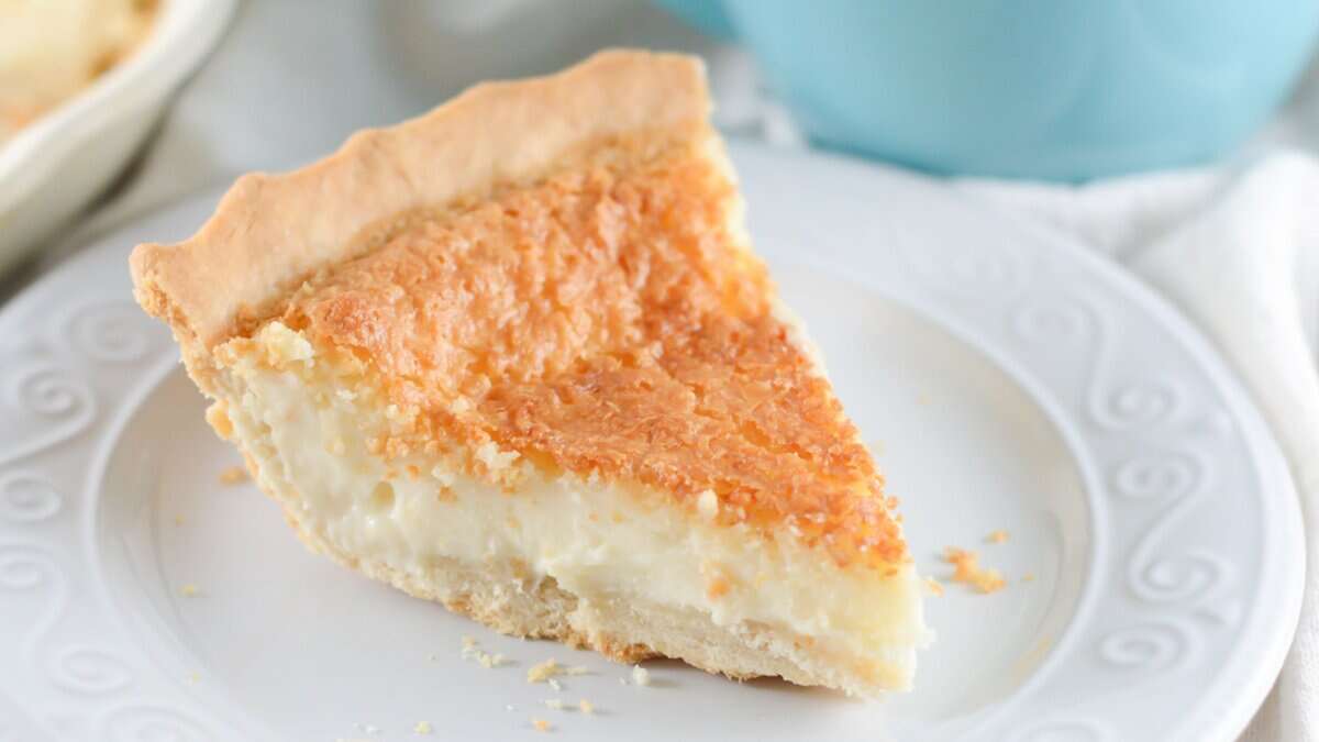 A slice of custard pie with a golden-brown top and flaky crust on a white plate&mdash;a perfect example of classic desserts.