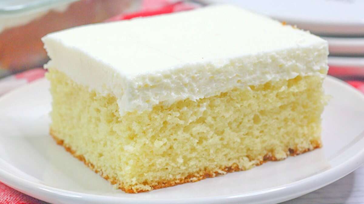 A slice of classic vanilla sheet cake with white frosting is served on a white plate, evoking the charm of traditional desserts.