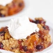A serving of Blueberry Peach Crisp topped with a scoop of vanilla ice cream on a white plate.