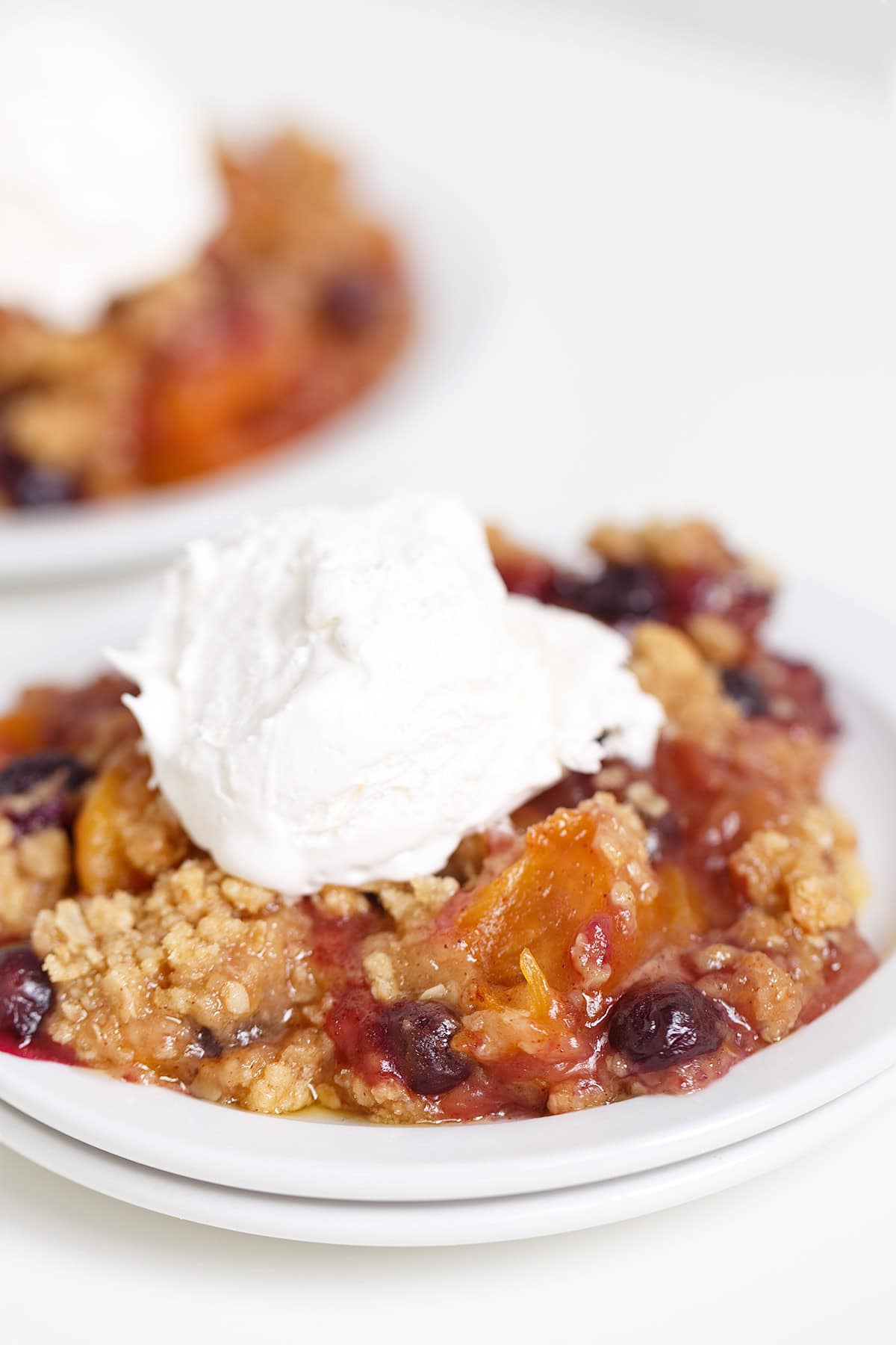 A serving of Blueberry Peach Crisp topped with a scoop of vanilla ice cream on a white plate.