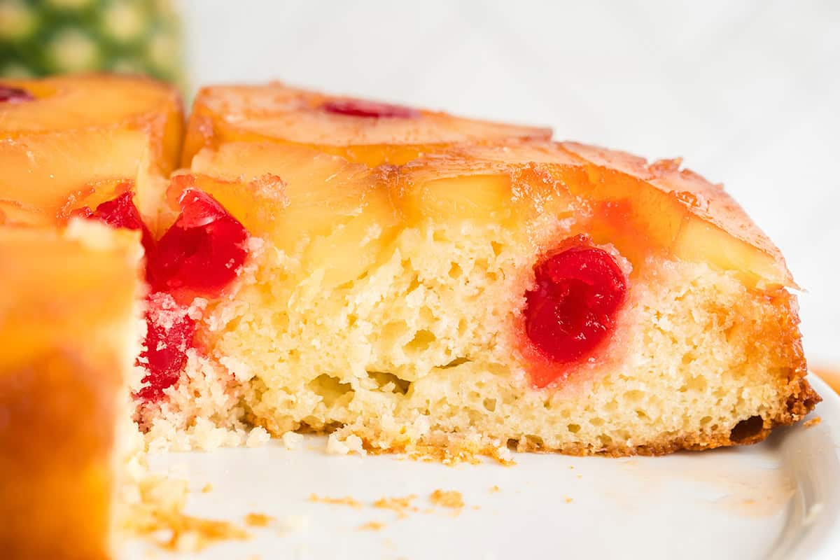 A close-up of a pineapple upside down cake made with cake mix, showing yellow pineapple rings and red cherries baked on top of a moist, light cake.