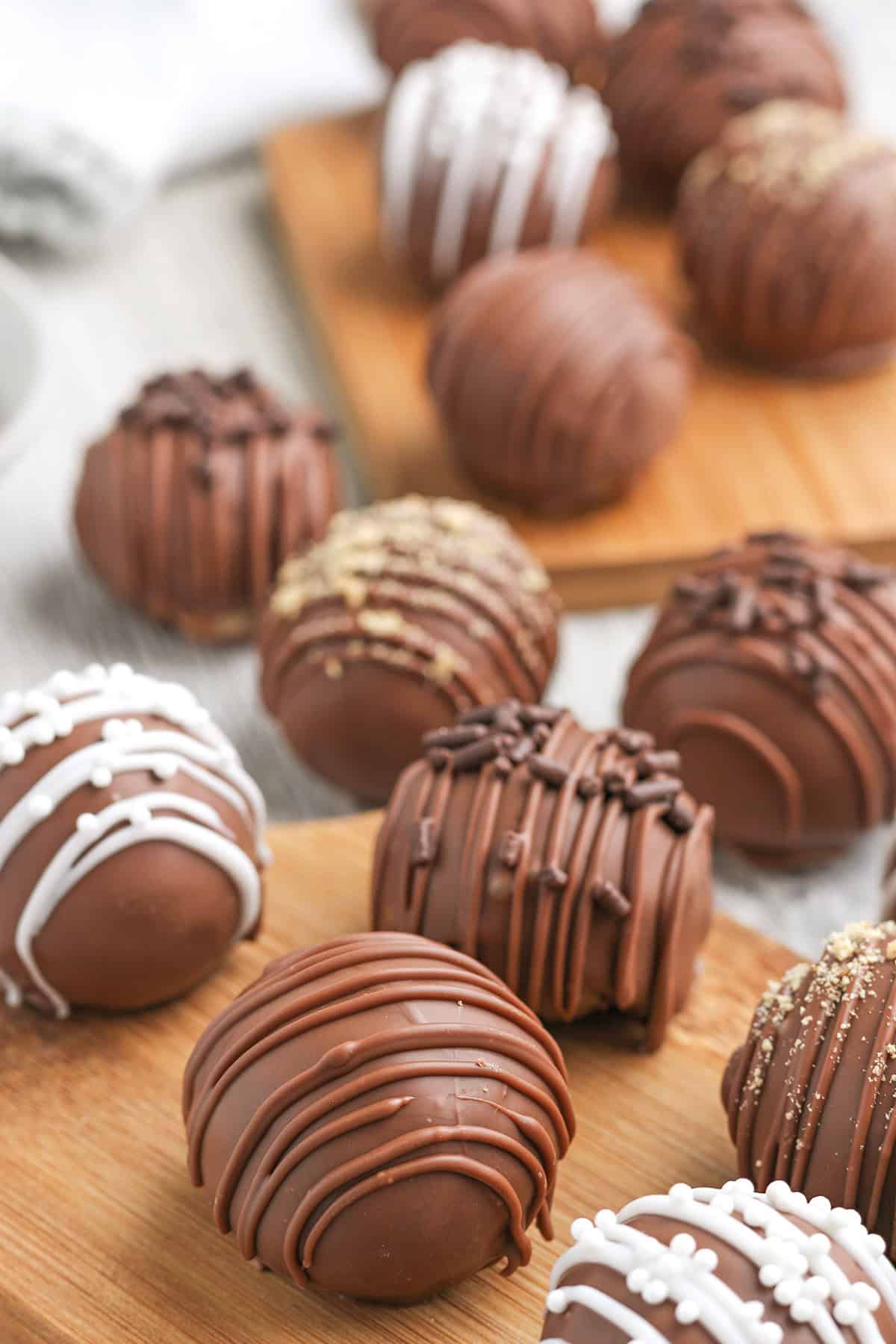 An assortment of chocolate truffles and cheesecake truffles, some drizzled with white or dark chocolate and others topped with sprinkles, arranged on wooden boards.