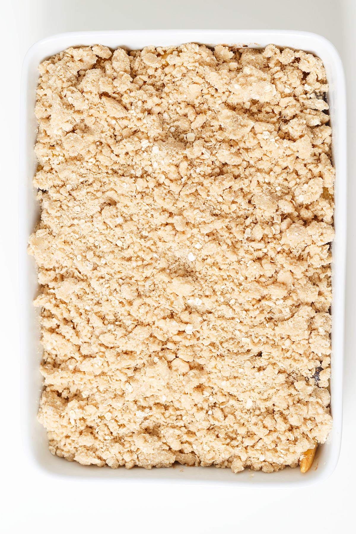A rectangular white dish filled with a layer of light brown crumbly mixture, perfect for a homemade Blueberry Peach Crisp or classic Peach Crisp, resembling a delicious streusel or crumb topping.