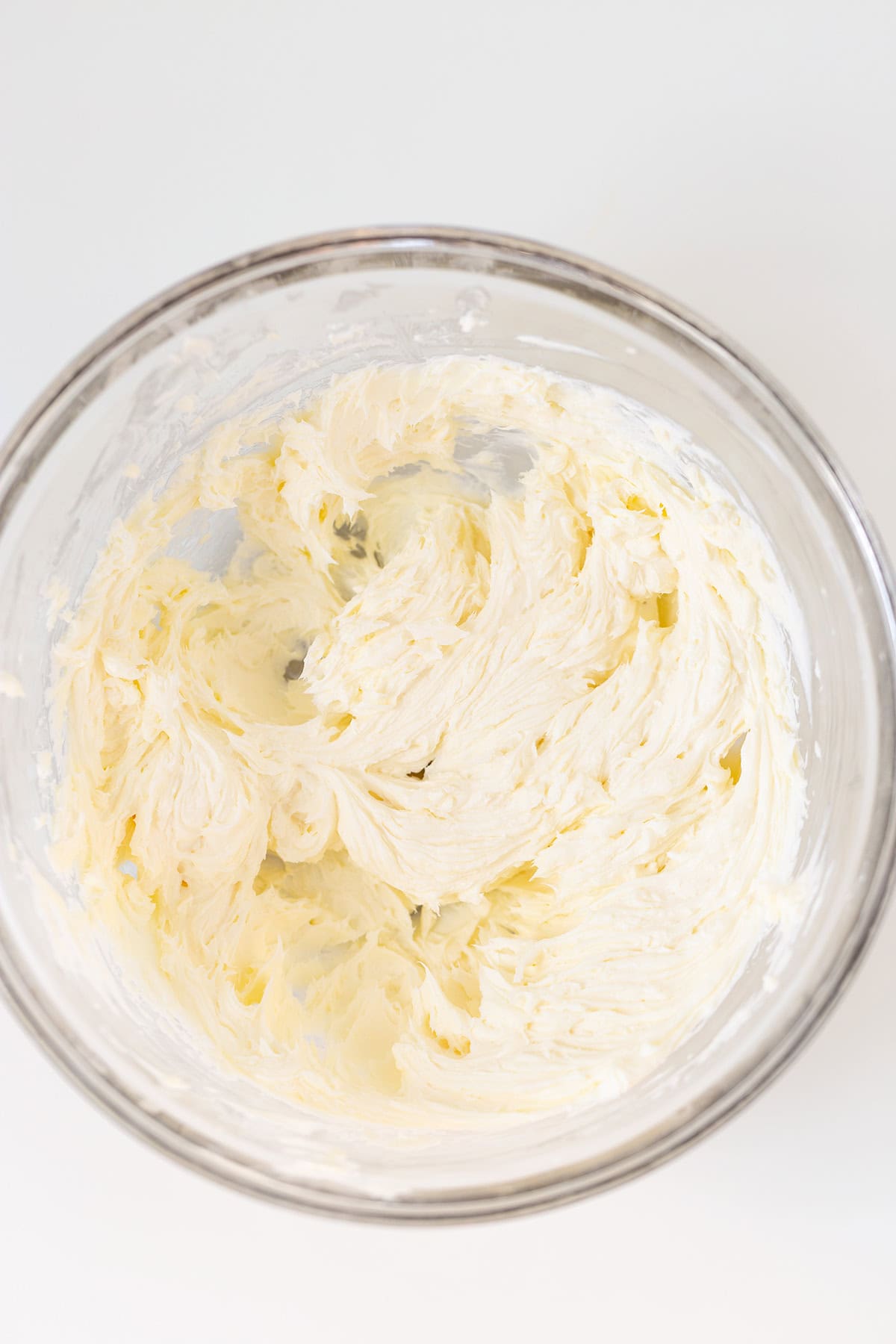 A glass mixing bowl containing a whipped, creamy Peanut Butter Dip mixture on a white surface.