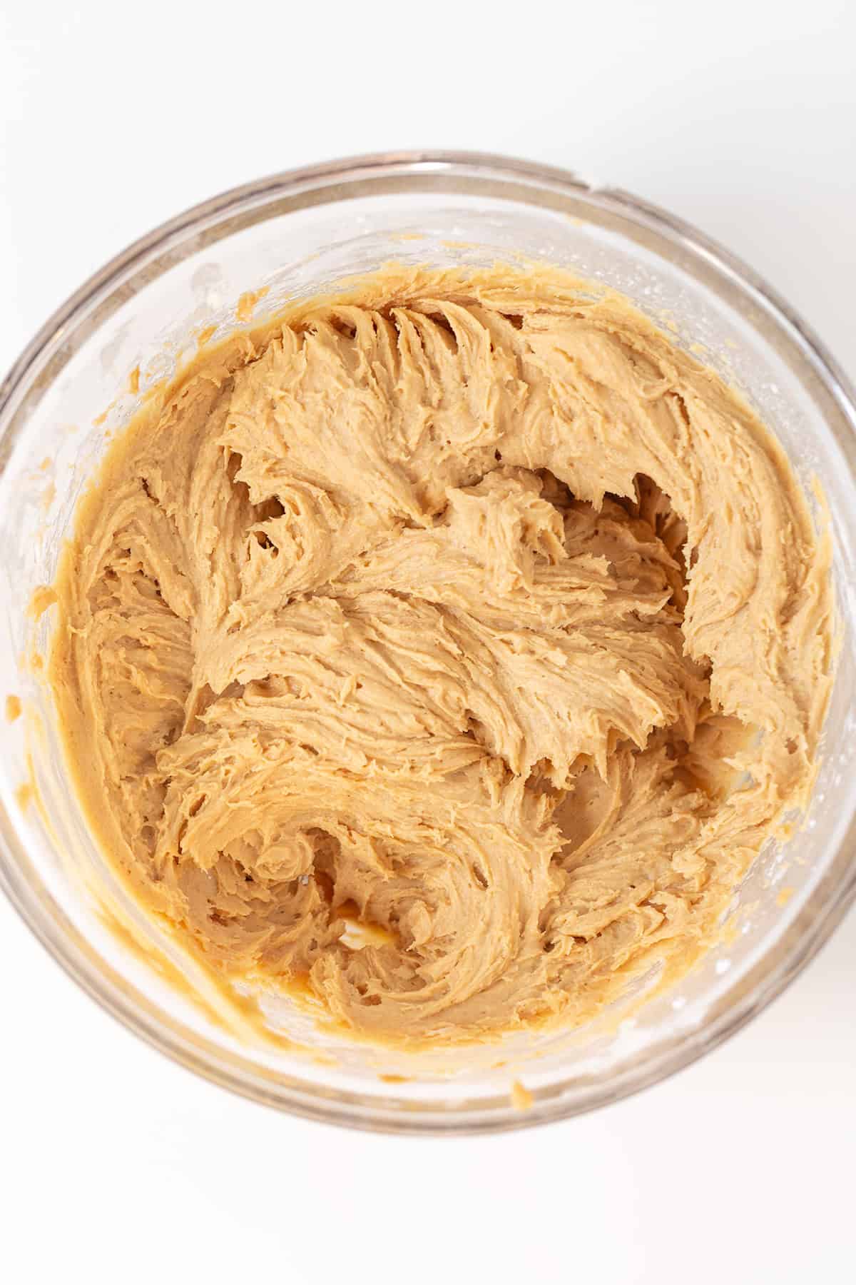 A glass bowl filled with creamy, light brown Peanut Butter Dip cookie dough sits on a white surface.