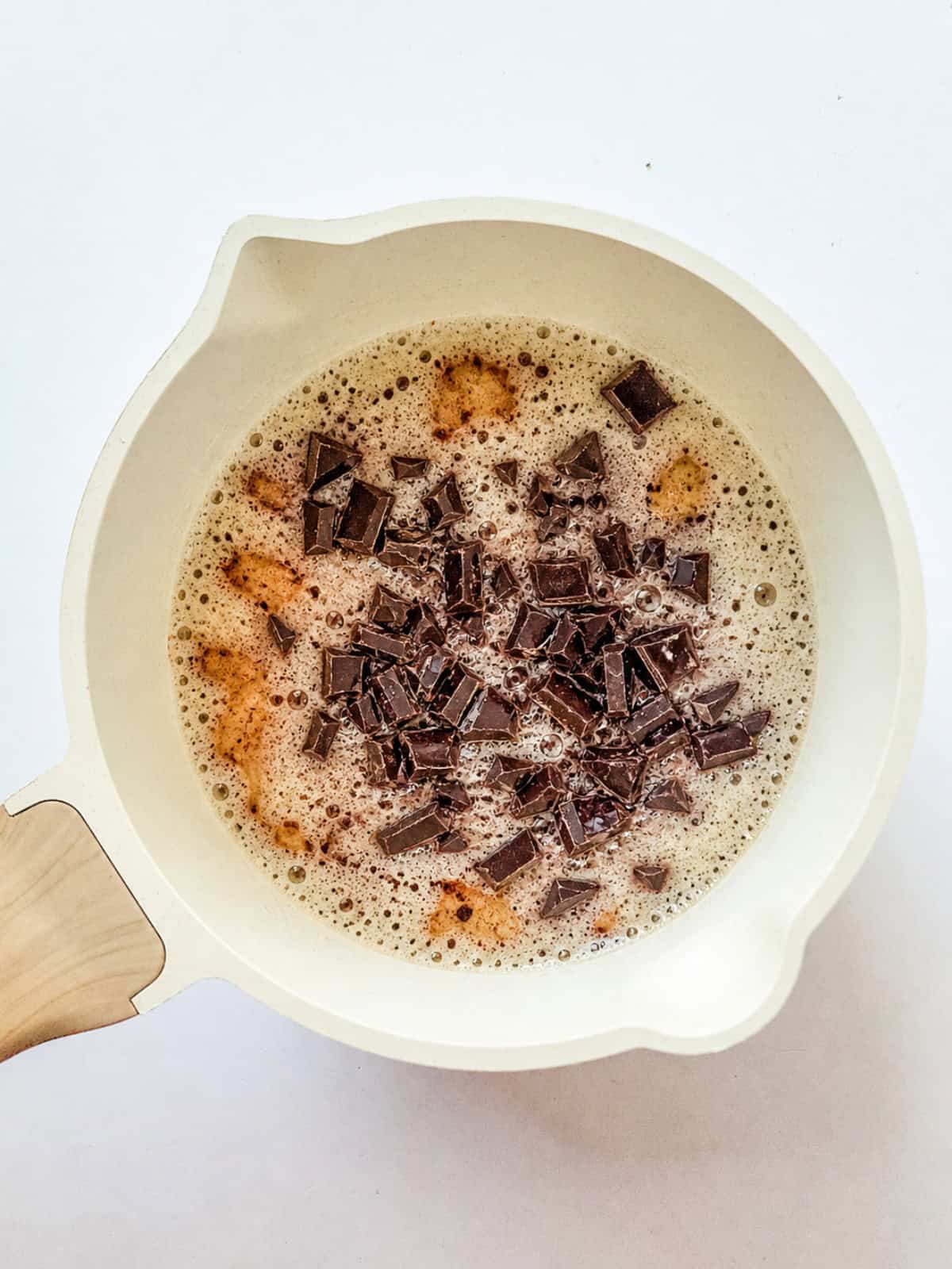 Chopped chocolate pieces melting in a saucepan with a frothy, light brown liquid, the perfect base for a rich Sweetened Condensed Milk Brownies recipe.