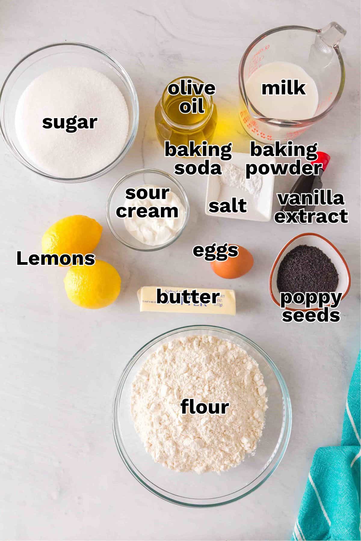 Bowls and containers with labeled ingredients for a Lemon Poppy Seed Bundt Cake: sugar, flour, lemons, butter, eggs, sour cream, olive oil, baking soda, baking powder, salt, milk, vanilla extract, and poppy seeds.