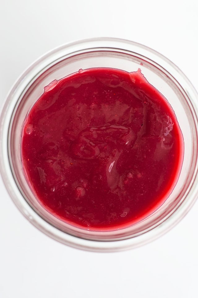 A close-up, overhead view of a jar filled with bright red cranberry sauce, reminiscent of a vibrant berry curd.